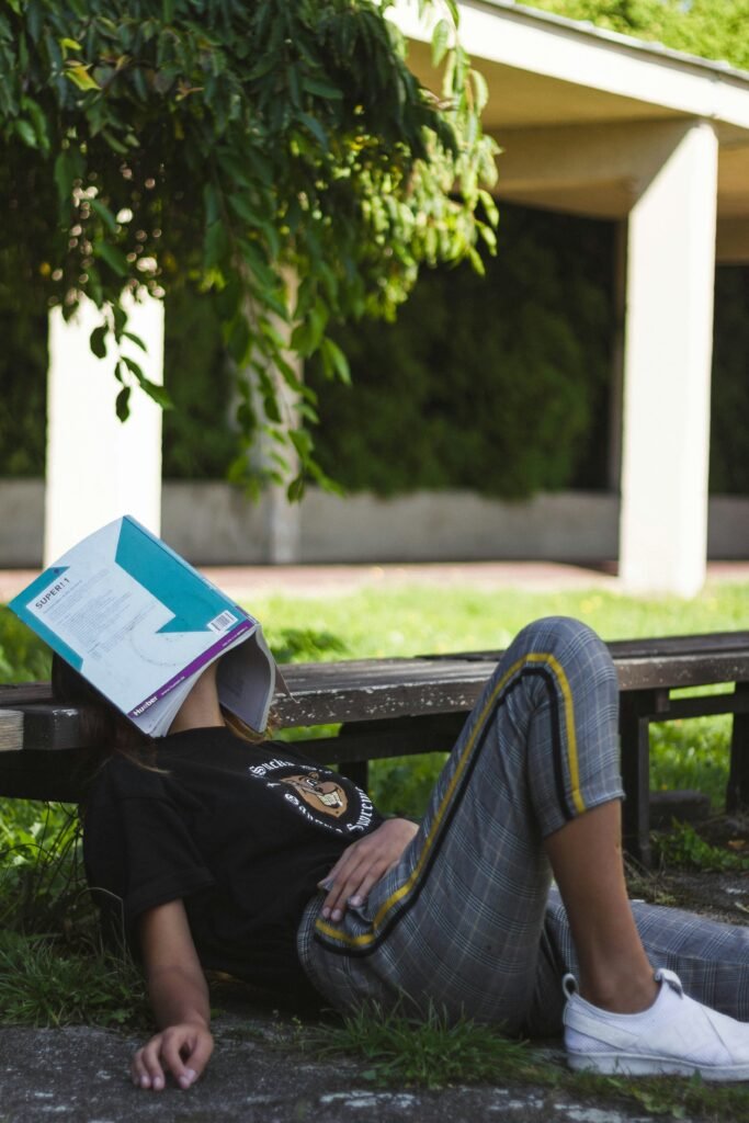 woman sitting against a bench with book laying over face; overwhelmed